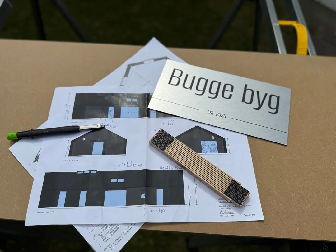 Byggetegninger, tommestok og Bugge Byg-skilt – planlægning af et byggeprojekt